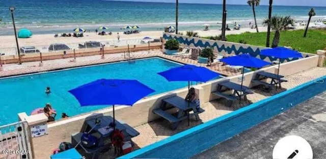 view of swimming pool with a view of the beach, a water view, and fence