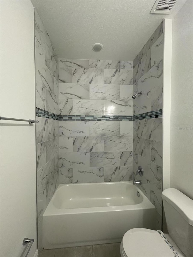 bathroom with toilet, a textured ceiling, and tiled shower / bath combo