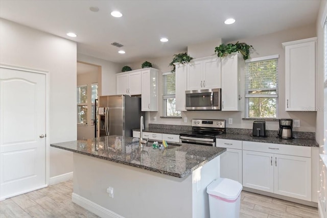 kitchen with light wood-type flooring, white cabinetry, a kitchen island with sink, and appliances with stainless steel finishes