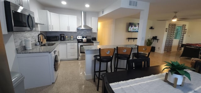 kitchen featuring decorative backsplash, appliances with stainless steel finishes, wall chimney exhaust hood, sink, and white cabinets