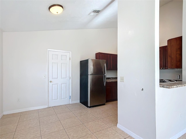 kitchen featuring light tile patterned flooring, dark brown cabinetry, vaulted ceiling, and stainless steel fridge