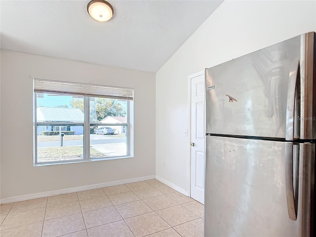 kitchen with stainless steel refrigerator, vaulted ceiling, and light tile patterned floors