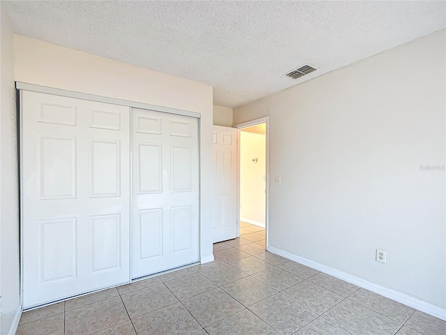 unfurnished bedroom featuring a textured ceiling, a closet, and light tile patterned floors