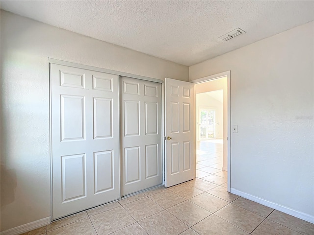 unfurnished bedroom featuring a textured ceiling, a closet, and light tile patterned floors