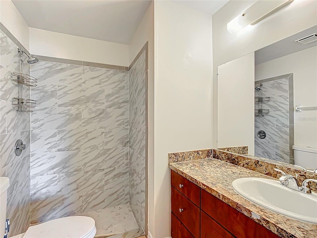 bathroom featuring a tile shower, vanity, and toilet