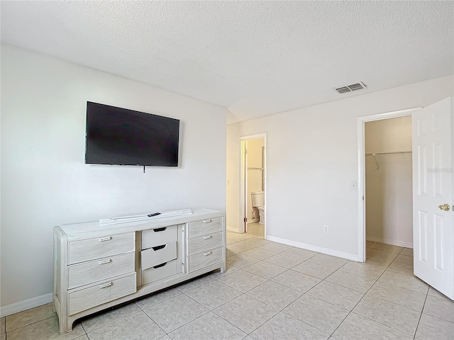 tiled bedroom with a textured ceiling, a walk in closet, a closet, and ensuite bath