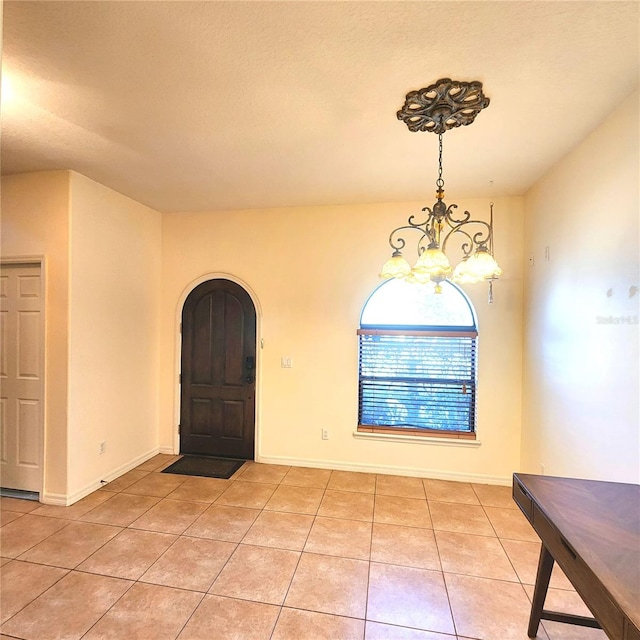 unfurnished dining area with light tile patterned flooring, a textured ceiling, and a notable chandelier