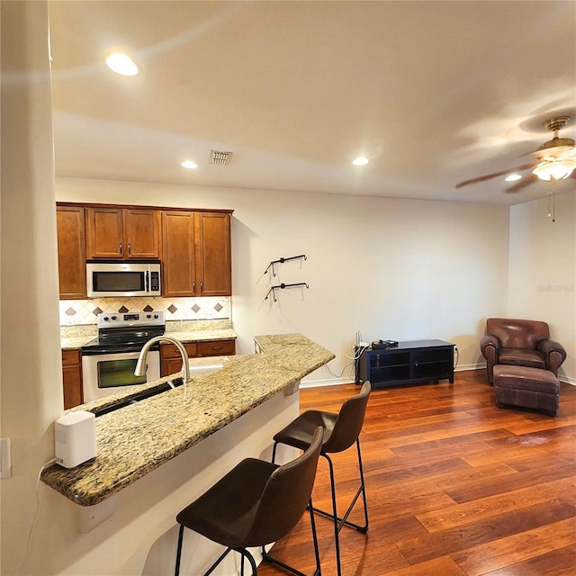 kitchen with a kitchen breakfast bar, tasteful backsplash, light stone counters, stainless steel appliances, and dark hardwood / wood-style floors