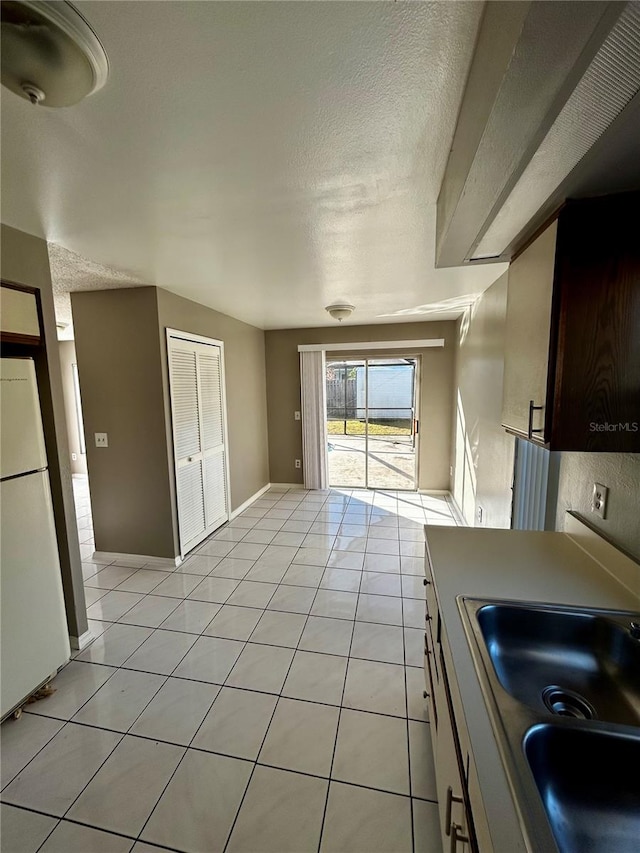 kitchen featuring light tile patterned floors, a textured ceiling, white fridge, and sink