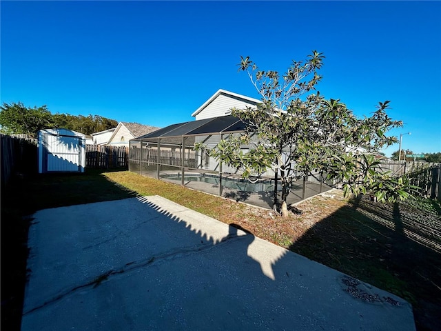 view of yard featuring a patio, a fenced in pool, a storage unit, and a lanai