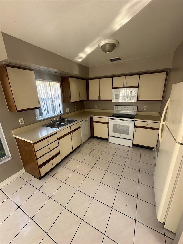 kitchen with cream cabinetry, light tile patterned flooring, white appliances, and sink