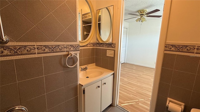 bathroom with ceiling fan, a textured ceiling, vanity, tile walls, and hardwood / wood-style flooring