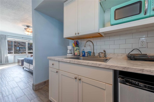 kitchen with white cabinetry, dishwasher, sink, tasteful backsplash, and light stone counters