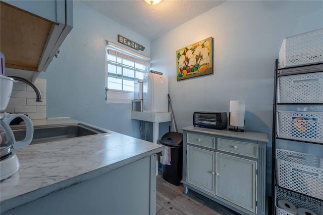 kitchen with decorative backsplash, gray cabinetry, a textured ceiling, sink, and light hardwood / wood-style flooring