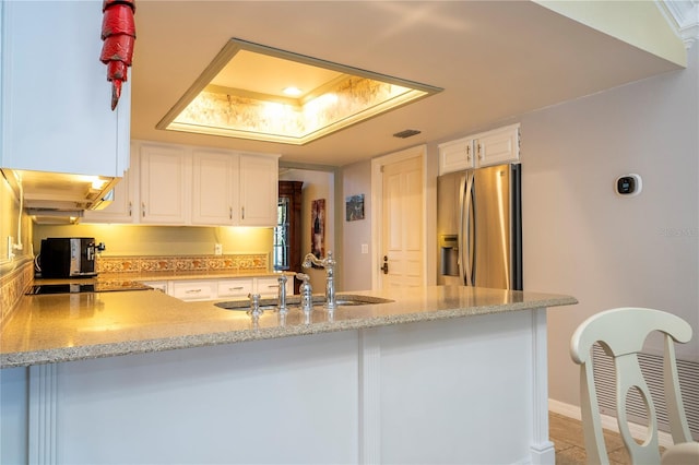 kitchen featuring kitchen peninsula, stainless steel fridge, a tray ceiling, sink, and white cabinetry