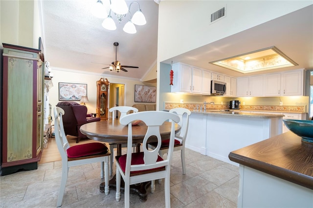 dining space with a skylight, high vaulted ceiling, crown molding, a textured ceiling, and ceiling fan with notable chandelier