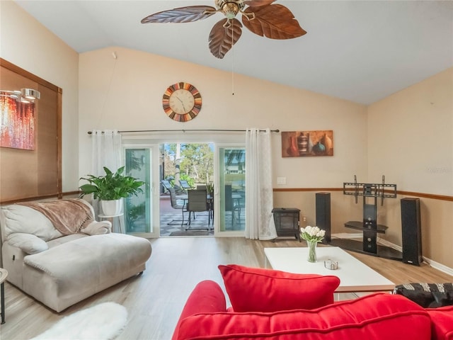 living room featuring a wood stove, ceiling fan, hardwood / wood-style floors, and vaulted ceiling