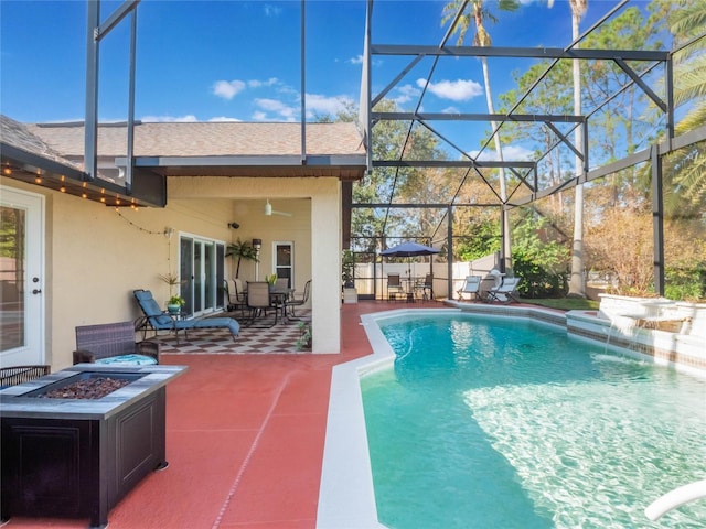 view of swimming pool with pool water feature, glass enclosure, a patio, and an outdoor fire pit