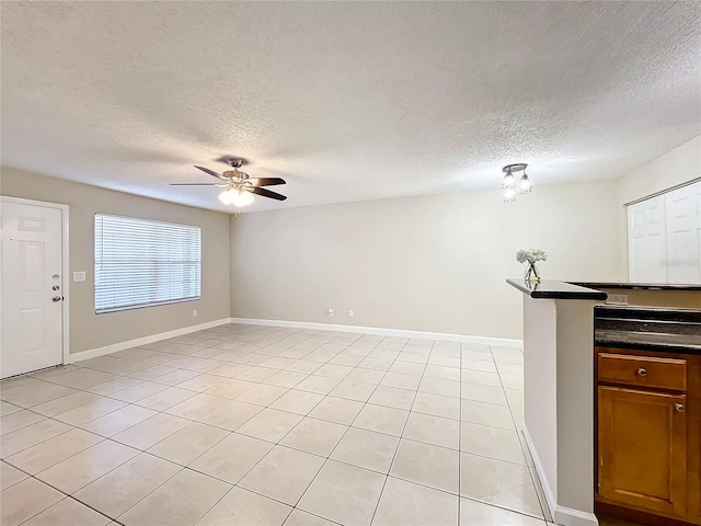 unfurnished living room featuring ceiling fan, light tile patterned floors, and a textured ceiling