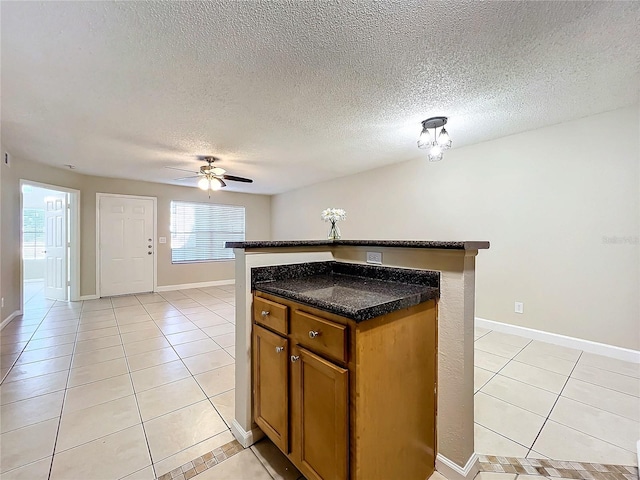 kitchen featuring light tile patterned floors, a textured ceiling, a center island, and dark stone counters