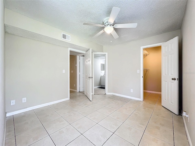 unfurnished bedroom featuring a walk in closet, ceiling fan, light tile patterned floors, a textured ceiling, and a closet