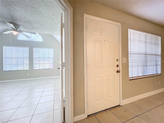 tiled entrance foyer with ceiling fan, a textured ceiling, and vaulted ceiling