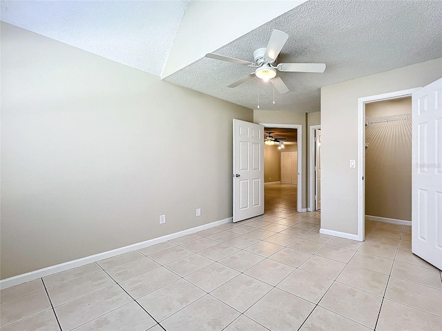 unfurnished bedroom featuring a walk in closet, ceiling fan, light tile patterned floors, a textured ceiling, and a closet