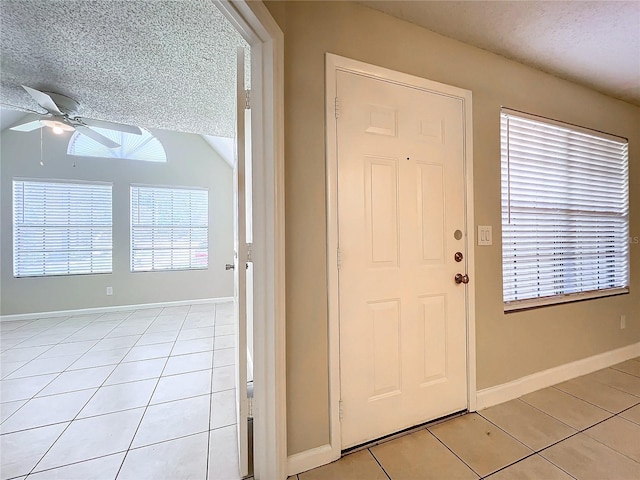 entrance foyer with light tile patterned floors, ceiling fan, a textured ceiling, and baseboards