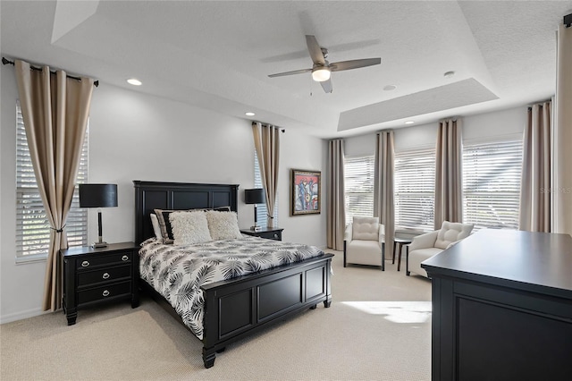 bedroom with ceiling fan, light colored carpet, and a tray ceiling