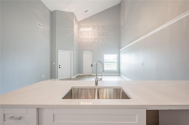 kitchen featuring lofted ceiling, sink, light wood-type flooring, decorative light fixtures, and white cabinetry