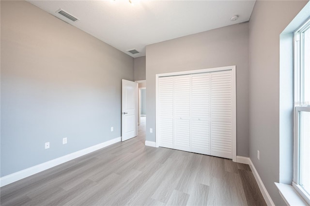 unfurnished bedroom featuring multiple windows, a closet, and light hardwood / wood-style flooring