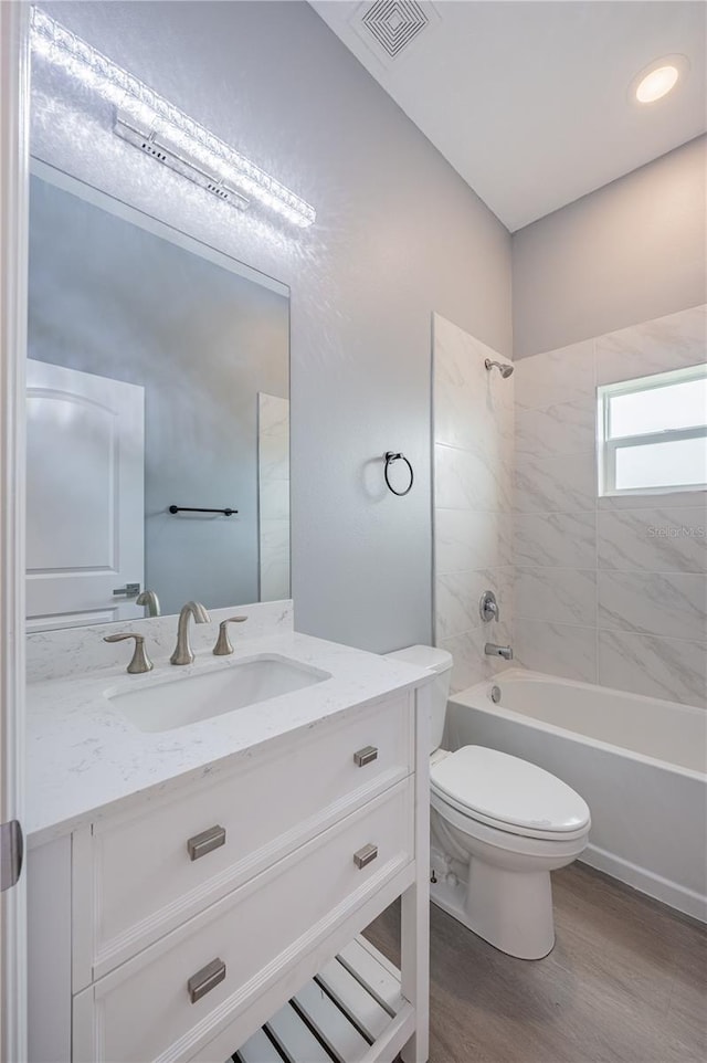 full bathroom featuring hardwood / wood-style floors, vanity, tiled shower / bath combo, and toilet