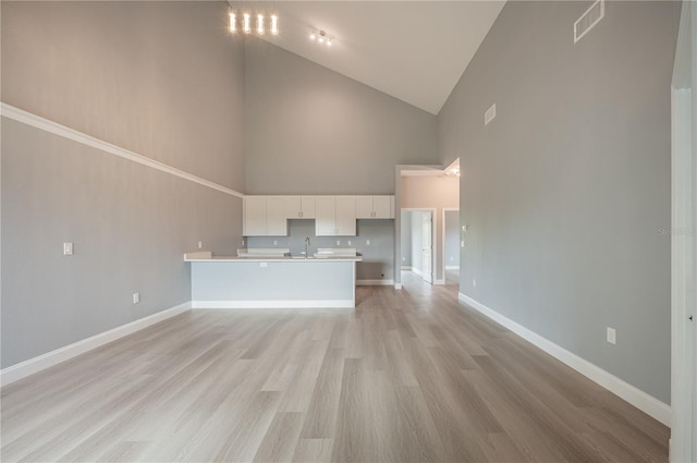 unfurnished living room featuring sink, high vaulted ceiling, and light hardwood / wood-style flooring