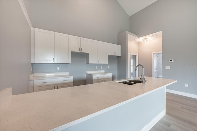 kitchen with white cabinets, light hardwood / wood-style floors, high vaulted ceiling, and sink