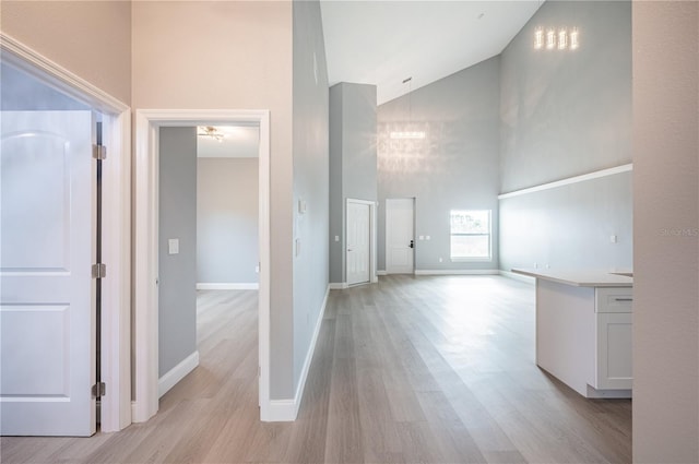 corridor with light hardwood / wood-style floors and high vaulted ceiling