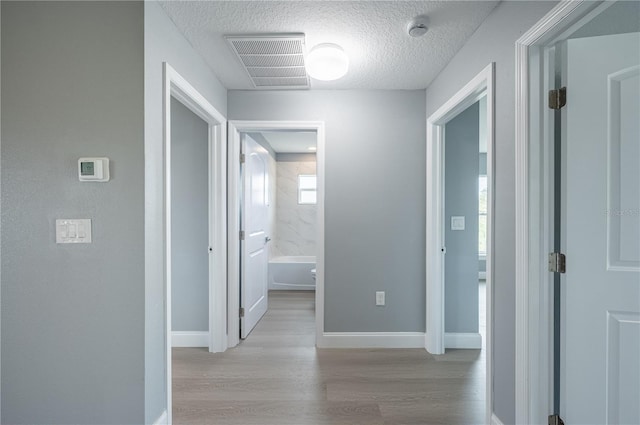 corridor featuring a textured ceiling and light hardwood / wood-style flooring