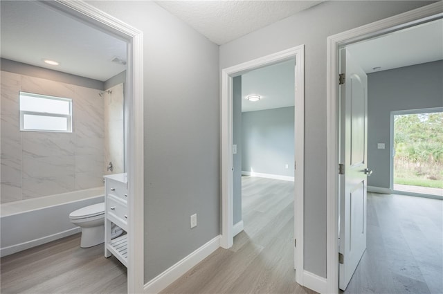 bathroom featuring toilet, a healthy amount of sunlight, tiled shower / bath combo, and wood-type flooring