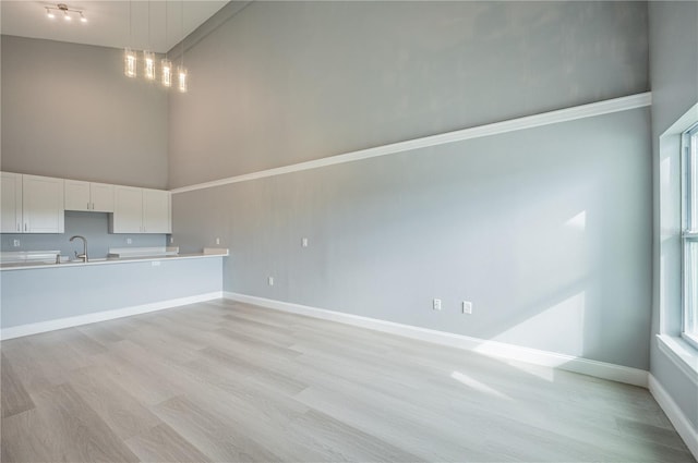 unfurnished living room with light hardwood / wood-style floors, high vaulted ceiling, and sink