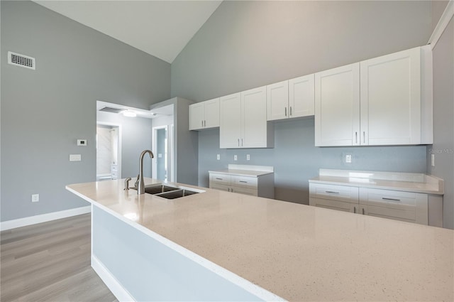 kitchen with white cabinetry, sink, light stone counters, high vaulted ceiling, and light hardwood / wood-style floors