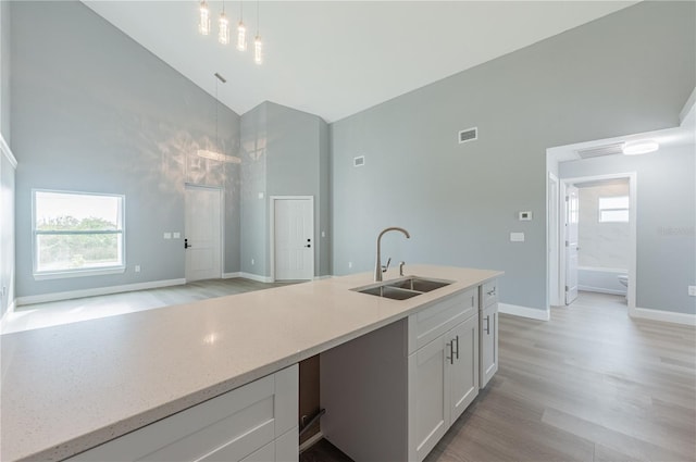 kitchen featuring sink, high vaulted ceiling, white cabinets, light hardwood / wood-style floors, and hanging light fixtures