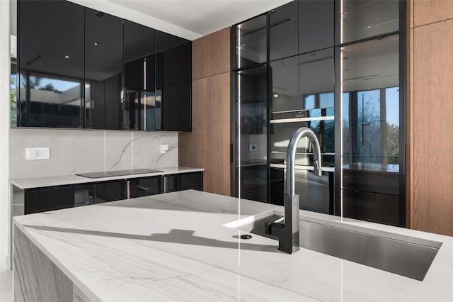 kitchen with decorative backsplash, light stone countertops, black electric cooktop, and sink