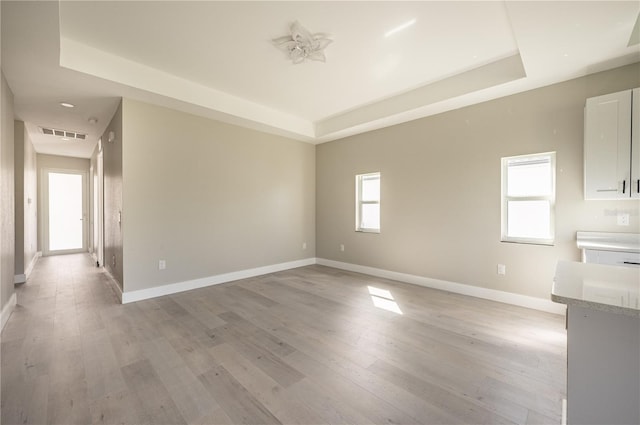 empty room with a raised ceiling and light hardwood / wood-style flooring