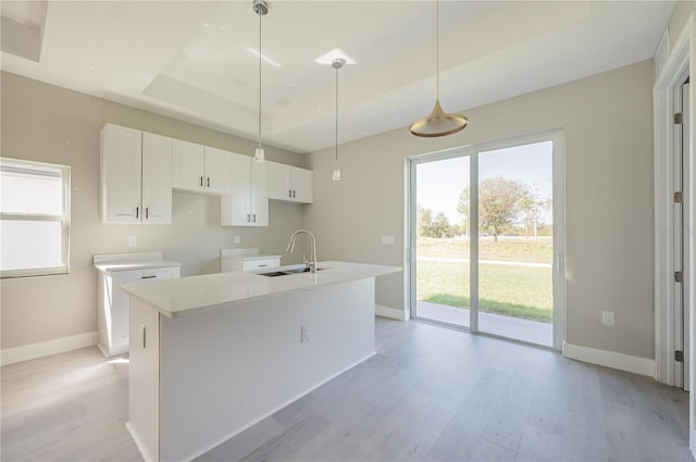 kitchen featuring sink, light hardwood / wood-style flooring, an island with sink, decorative light fixtures, and white cabinets