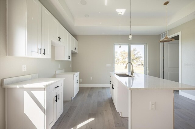 kitchen featuring sink, white cabinets, decorative light fixtures, and a center island with sink