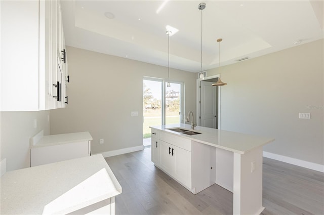 kitchen featuring sink, hanging light fixtures, an island with sink, white cabinets, and light wood-type flooring