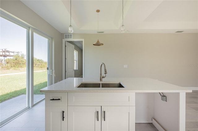 kitchen featuring a kitchen island with sink, sink, white cabinets, light hardwood / wood-style floors, and hanging light fixtures