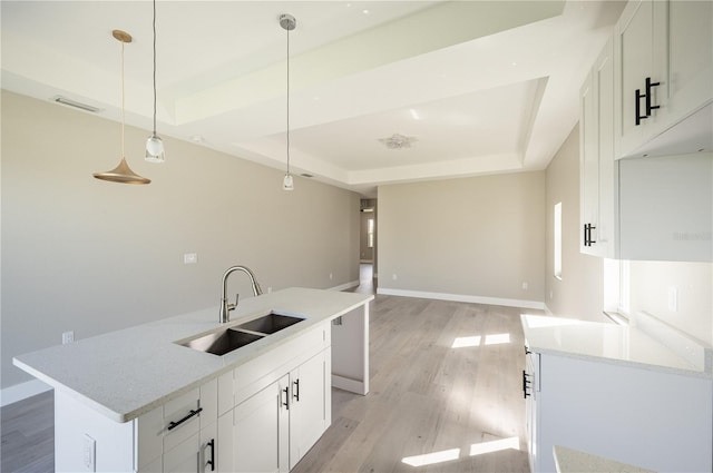 kitchen with a raised ceiling, white cabinetry, sink, and decorative light fixtures