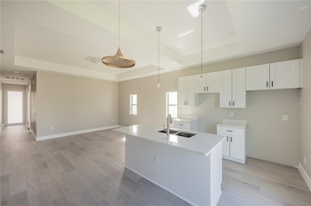 kitchen featuring a tray ceiling, sink, decorative light fixtures, white cabinets, and an island with sink