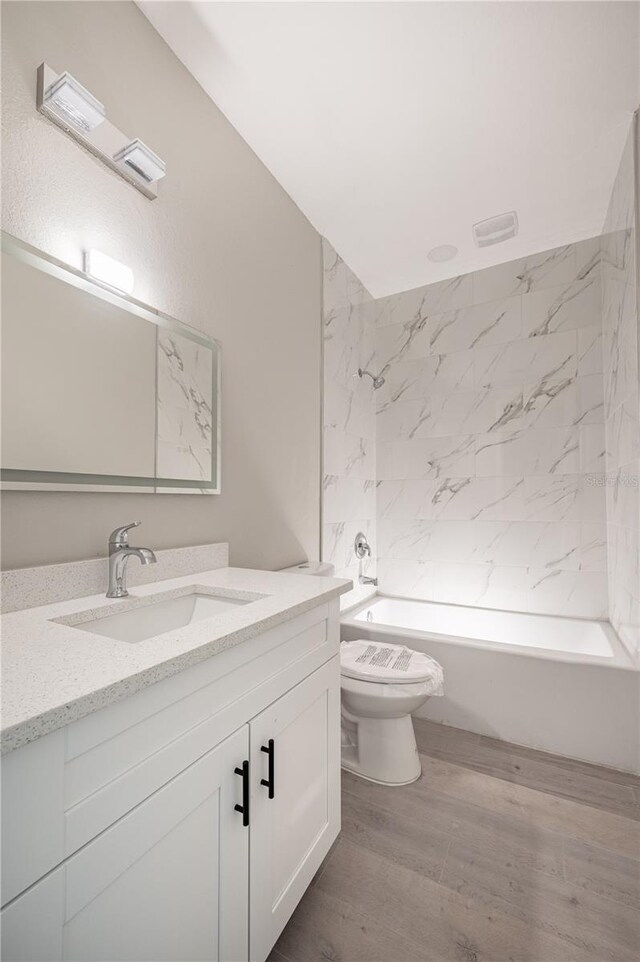 full bathroom with hardwood / wood-style flooring, vanity, toilet, and tiled shower / bath