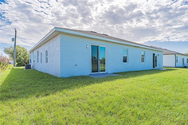 rear view of house with central air condition unit and a lawn